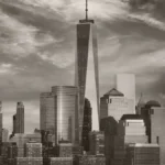 Grayscale New York City skyline with One World Trade Center towering above surrounding skyscrapers, under a cloudy sky.