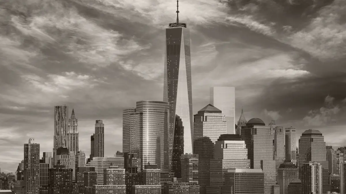 Grayscale New York City skyline with One World Trade Center towering above surrounding skyscrapers, under a cloudy sky.