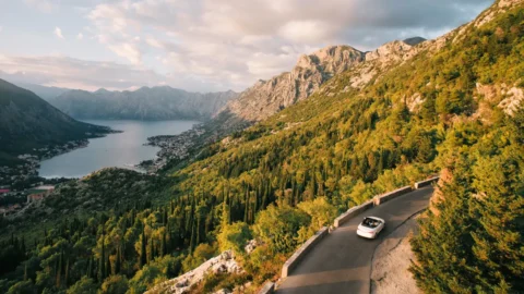 What High-Net-Worth Individuals Get Wrong About Tax Planning | Rhame & Gorrell Wealth Management White car drives along a curving mountain road with a lake and town visible in the valley below.