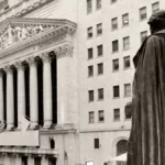 Bronze statue in the foreground with a cloaked back, facing a grand neoclassical courthouse with tall columns and flags in the background.
